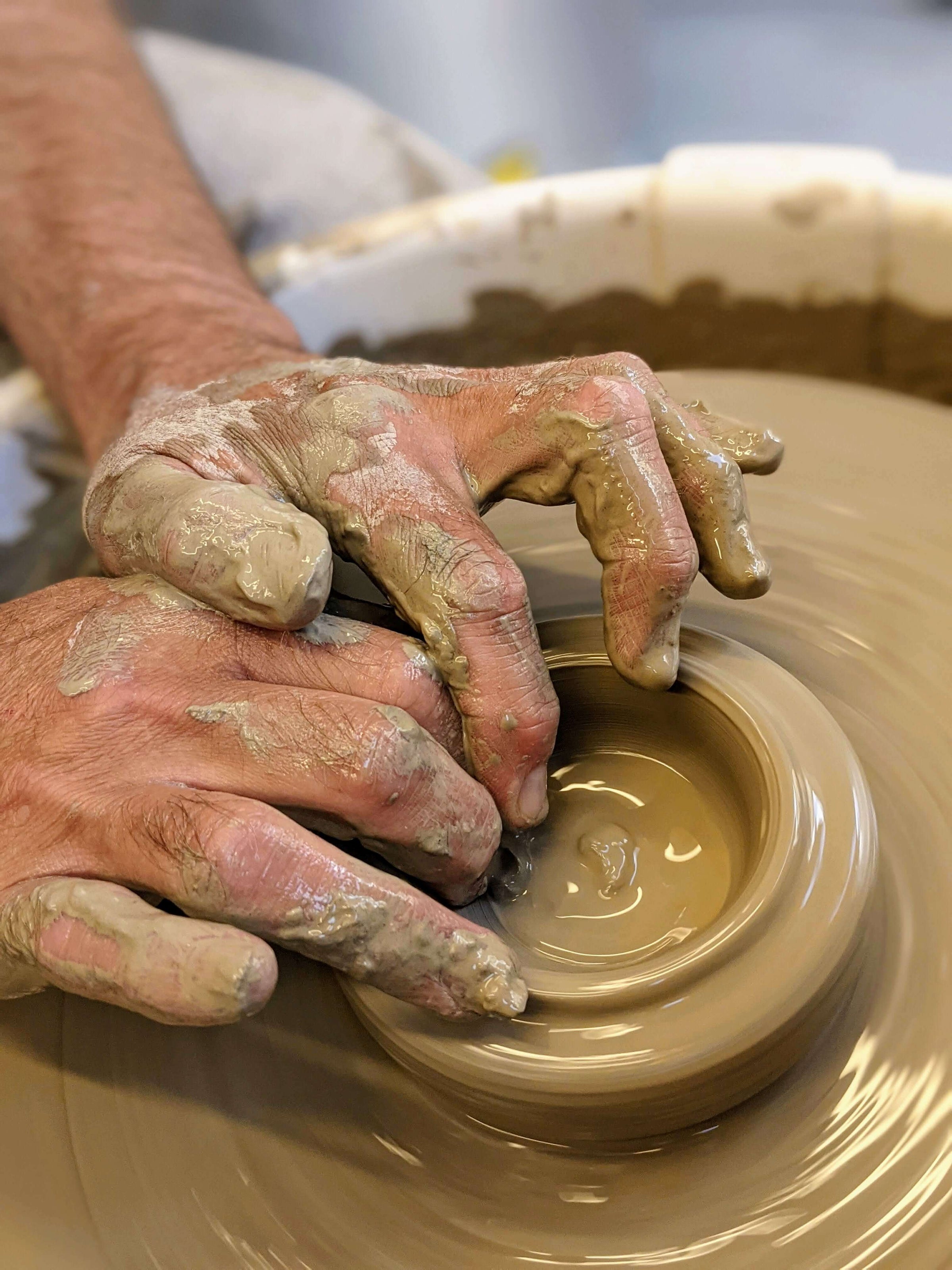 A detailed image of a pair of hands delicately sculpting clay on a potter's  wheel during a soft-lit evening in a pottery studio, captured with a medium  format camera using a macro
